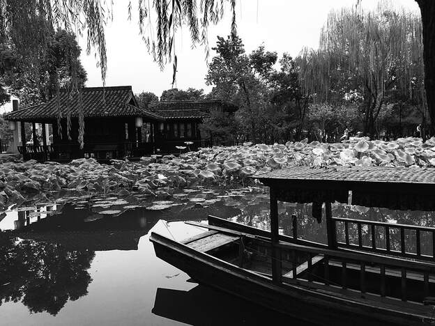 Photograph of pond with Chinese sampan in foreground. In background, a thicket of Lilly pads and a Chinese pagoda on the distance shore. 